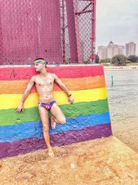 Full length of shirtless man standing by colorful wall