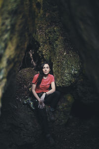 Full length portrait of young woman leaning on rock in forest