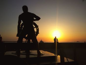 Silhouette men standing by sea against sky during sunset