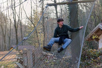 An amused caucasian boy lands on a safety net of an adventure park