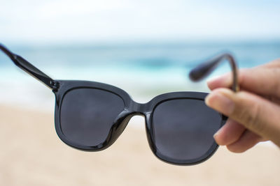 Close-up of hand holding sunglasses against sea
