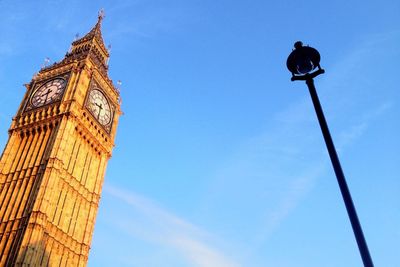 Low angle view of big ben and street lamp against blue sky