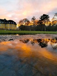 Scenic view of lake by buildings against sky during sunset