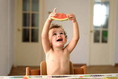 Shirtless girl holding watermelon at home