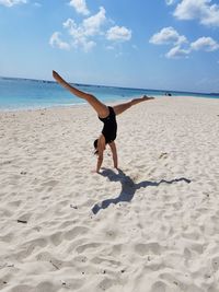 Full length of teenage girl doing handstand at beach against sky