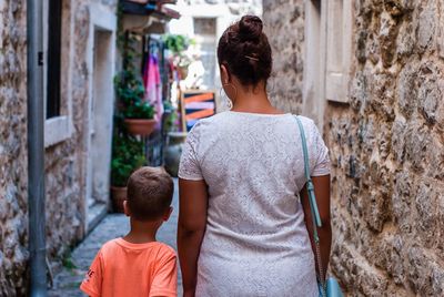 Rear view of mother and son walking in alley