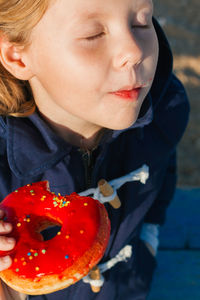 Girl in delight eats donut with red icing, food stained her mouth