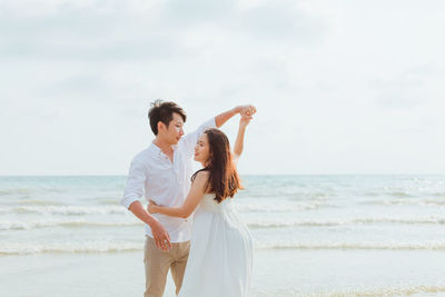 Couple standing at beach against sky