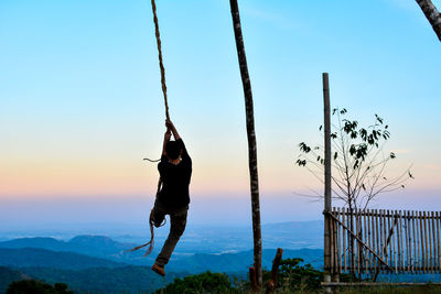 Rear view of man playing on rope against sky