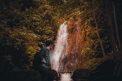 Young man looking at waterfall while standing in forest