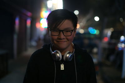 Portrait of smiling boy with headphones standing in city at night