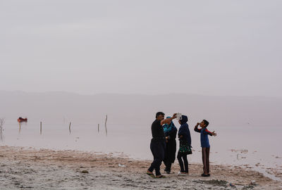 People standing on beach against clear sky