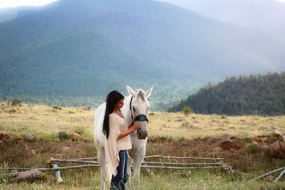 Woman touching horse while standing on grassy field