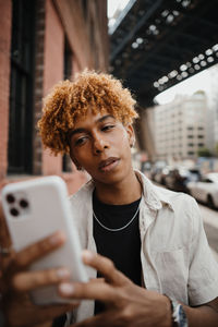 Active mixed race teenager smiling and typing message at the smartphone while walking at the city