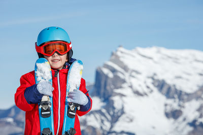 Portrait of young man wearing warm clothing standing against snowcapped mountain