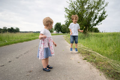 Siblings standing on road against sky