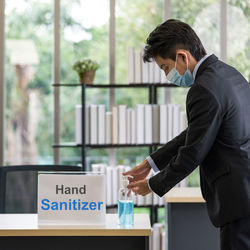 Side view of a young man with mask pouring sanitizer in hand