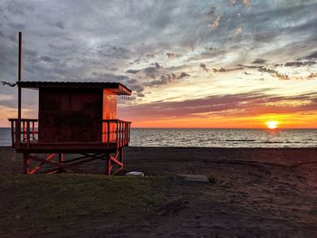 Hut on beach against sky during sunset