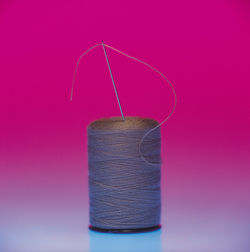 Close-up of thread and needle over colored background