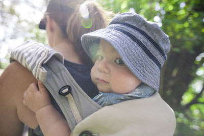 Portrait of son being carried by mother in baby carrier at forest