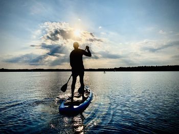Rear view of man standing in boat on lake against sky during sunset