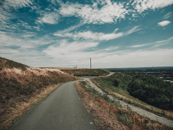 Country road amidst landscape against sky