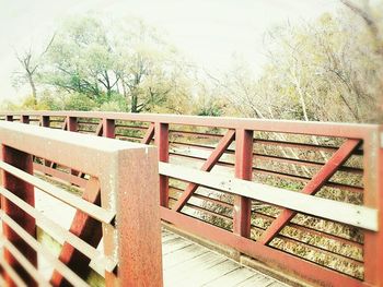 Wooden railing by trees against sky