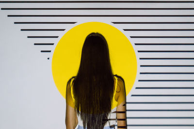 Back view of unrecognizable woman with long hair in yellow projector light with stripes