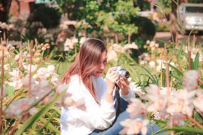 Woman photographing by flowering plants at park