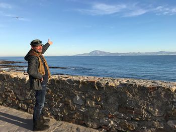 Man standing by retaining wall at beach against sky