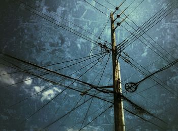 Low angle view of electricity pylon against cloudy sky