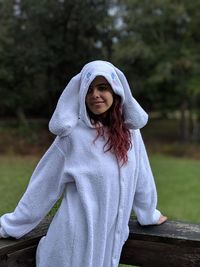 Portrait of young woman wearing white warm clothing while standing against trees