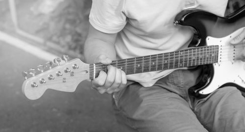 Black and white photo of a young guy playing guitar, close-up, focus on fingers.