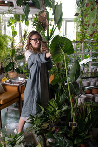 Cheerful woman with mobile phone standing against plants