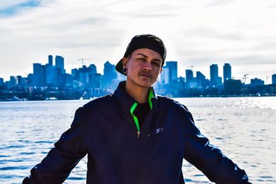 Portrait of young man standing against sea in city