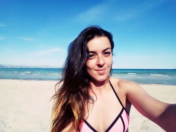 Portrait of young woman wearing bikini at beach against blue sky on sunny day