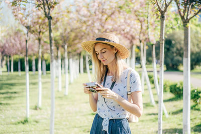 Young beautiful stylish woman photographer in a hat with a digital camera in a city park.