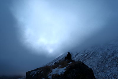 Scenic view of  a man sitting on a rock against the snow mountain  and foggy sky