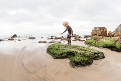 Toddler boy standing on green rock at a beach in new zealand