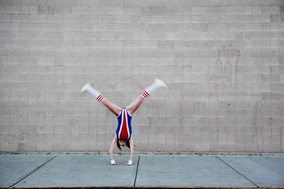 Woman in old-fashioned sports costume doing cartwheel on sidewalk against wall