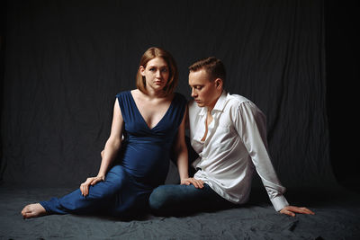 Young couple sitting against black background