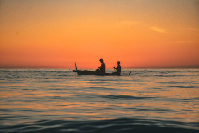 Silhouette people in sea against sky during sunset