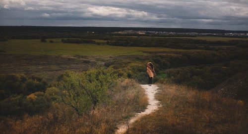 Rear view of woman on landscape against cloudy sky