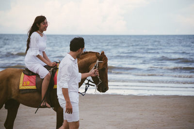 Young woman with boyfriend riding horse at beach