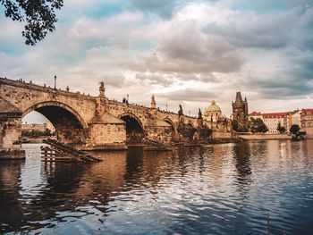 Arch bridge over river against cloudy sky