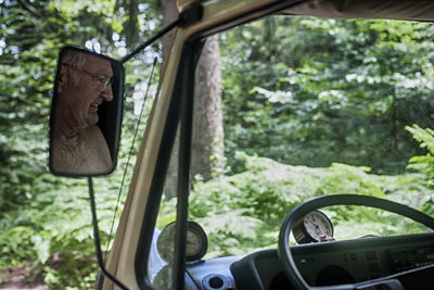 Reflection of smiling senior man on side-view car mirror in forest