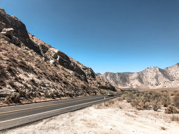 Road leading towards mountains against clear blue sky