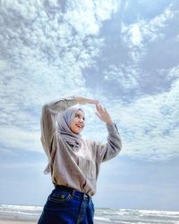 Young woman standing by sea against sky