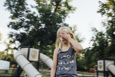 Girl with eyes closed standing against sky in playground
