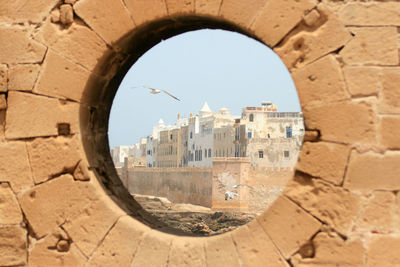 Buildings and bird seen through hole on sunny day